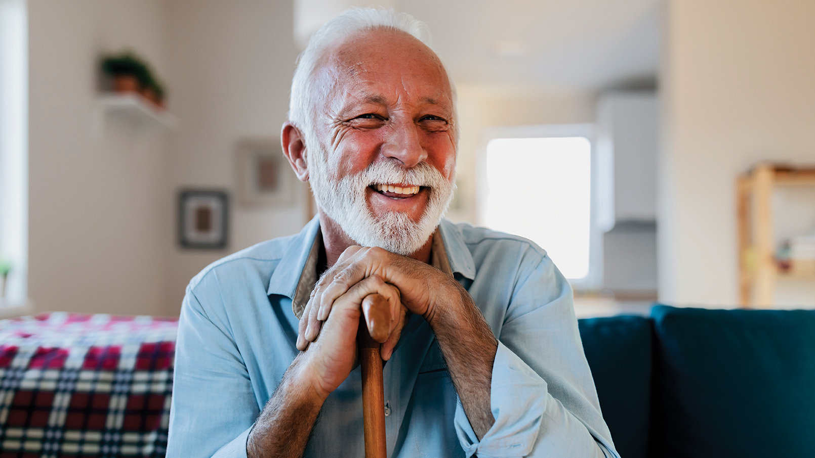 Beautiful bearded smiling older man holding a cane while sitting on a couch.