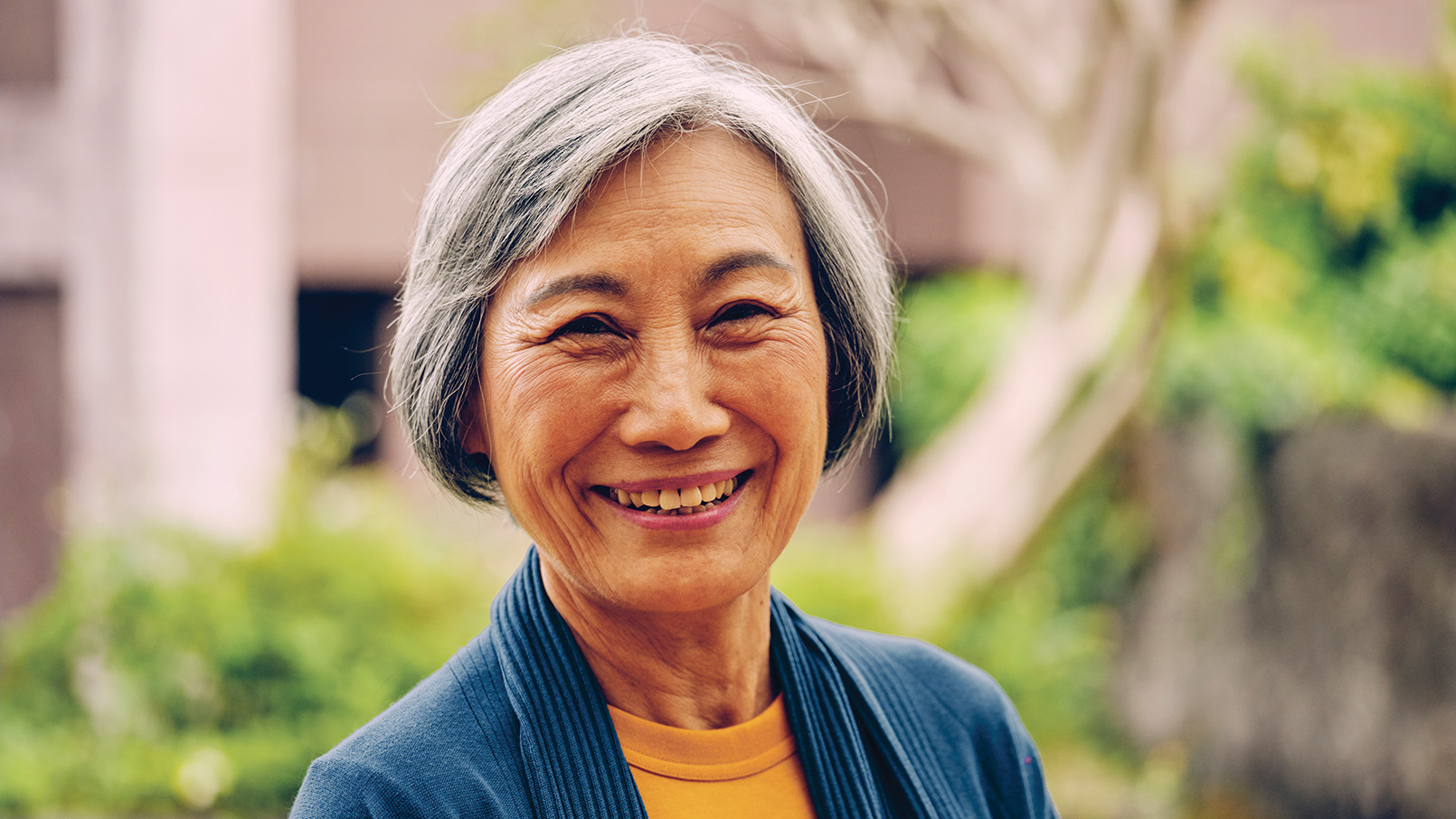 Smiling older lady in a garden surrounded by vibrant flowers and greenery.
